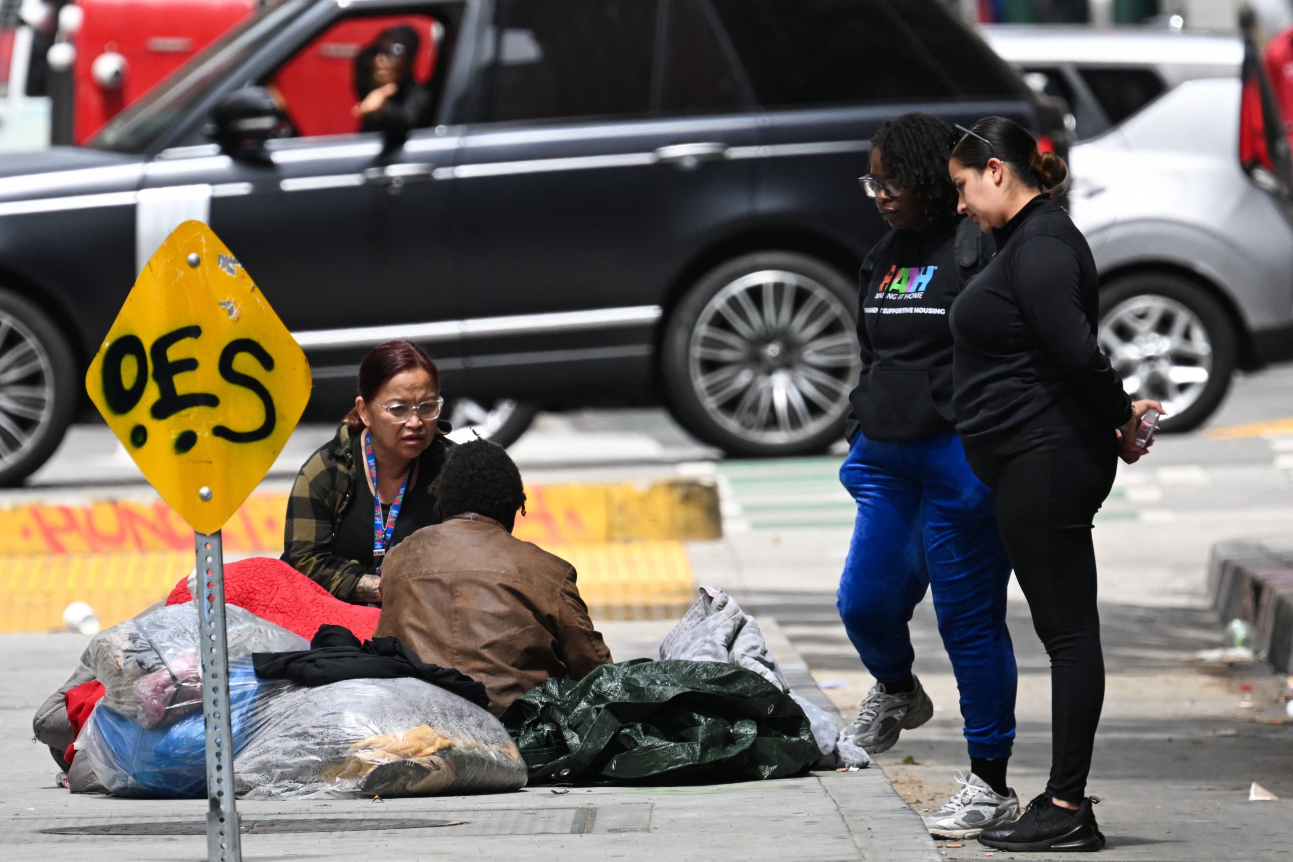 An homeless outreach representative with PATH speaks with a person experiencing homelessness sitting on the street in downtown Los Angeles, California on May 1, 2025. (Photo by PATRICK T. FALLON/AFP via Getty Images)