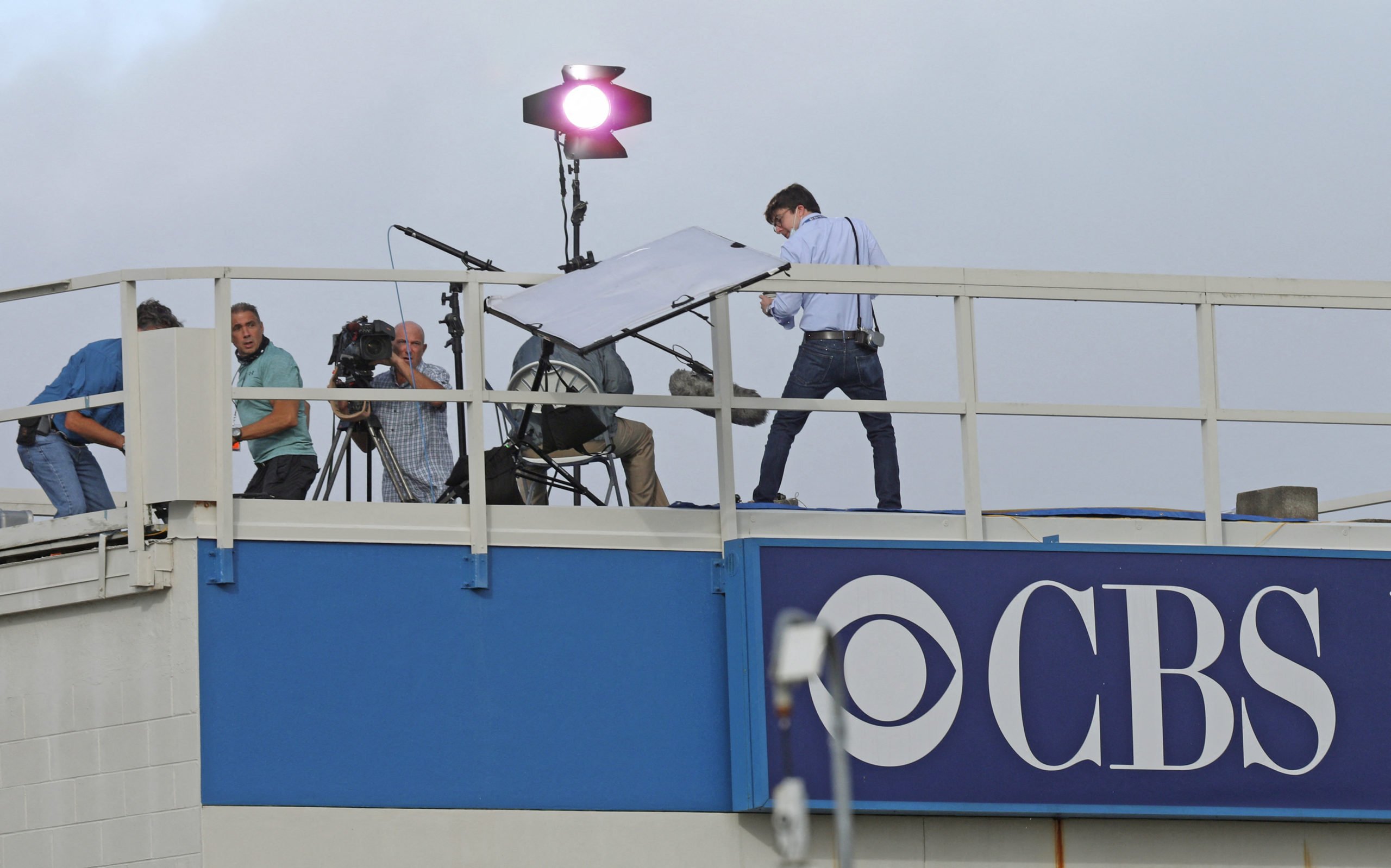 A CBS News crew looks on as a reflector topples over from the wind while preparing to broadcast. (Photo by GREGG NEWTON/AFP via Getty Images)