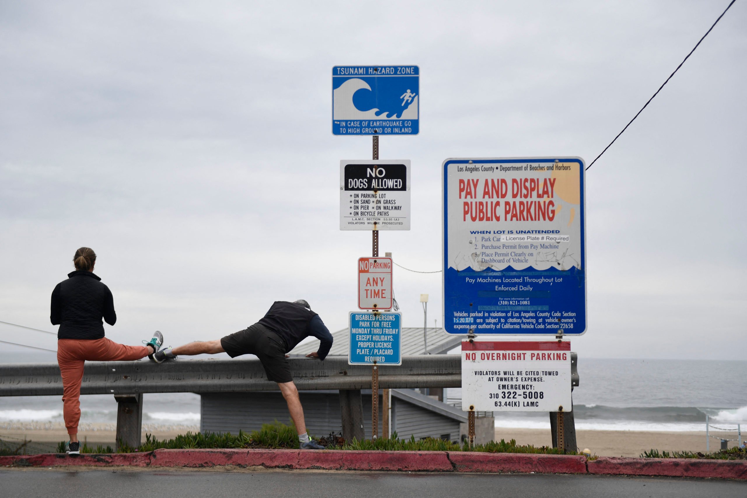People stretch next to a tsunami hazard zone sign in El Segundo, California, on January 15, 2022 (Photo by PATRICK T. FALLON/AFP via Getty Images)