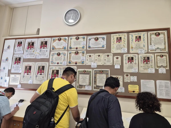 Visitors inspect signs hanging in the office of papal charities in Vatican City showing the different models of papal blessing certificates that can be ordered, Tuesday, July 29, 2025. Credit: Hannah Brockhaus/CNA