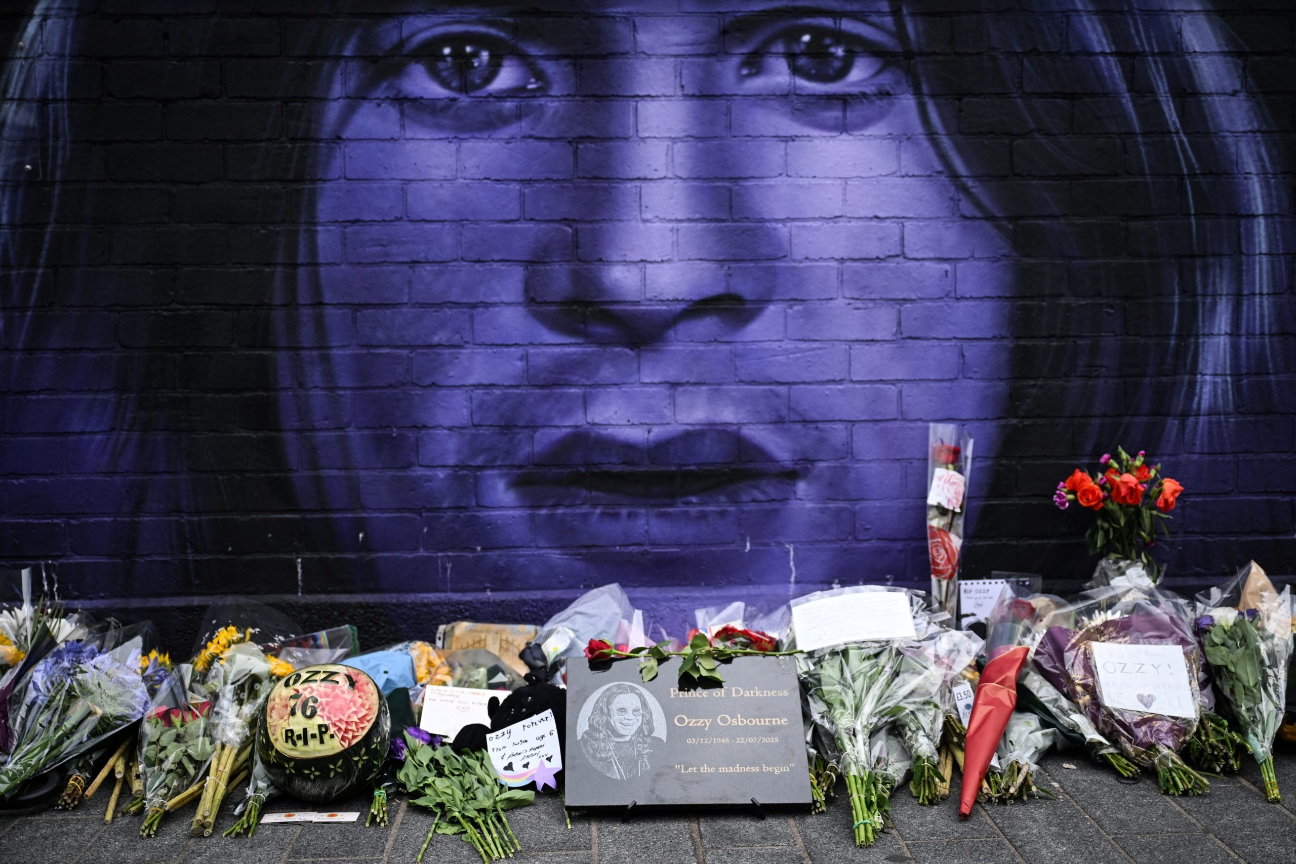 TOPSHOT - A photograph taken on July 23, 2025 shows flowers, candles and drawings left at a makeshift memorial by a mural depicting late British singer-songwriter Ozzy Osbourne, in Birmingham, central England, a day after his death. Tributes poured in on July 23, 2025 for hell-raiser singer Ozzy Osbourne as tearful fans laid flowers in his hometown and his Black Sabbath band mates mourned the death of their legendary heavy metal frontman, just weeks after he played an epic farewell concert in their Birmingham hometown. Osbourne, nicknamed the