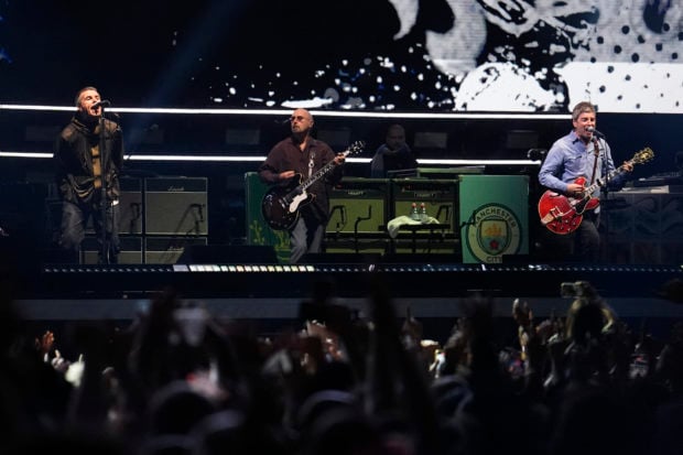 (L-R) Liam Gallagher, lead singer, Paul Arthurs, rhythm guitarist, and Noel Gallagher, lead guitarist of British rock band Oasis perform on stage at the Principality Stadium in Cardiff on July 4, 2025, during the opening concert of their highly anticipated reunion tour nearly 16 years after last performing together. (Photo by AFP stringer / AFP) / RESTRICTED TO EDITORIAL USE - NOT TO BE USED AFTER JULY 3, 2026 (Photo by AFP STRINGER/AFP via Getty Images)