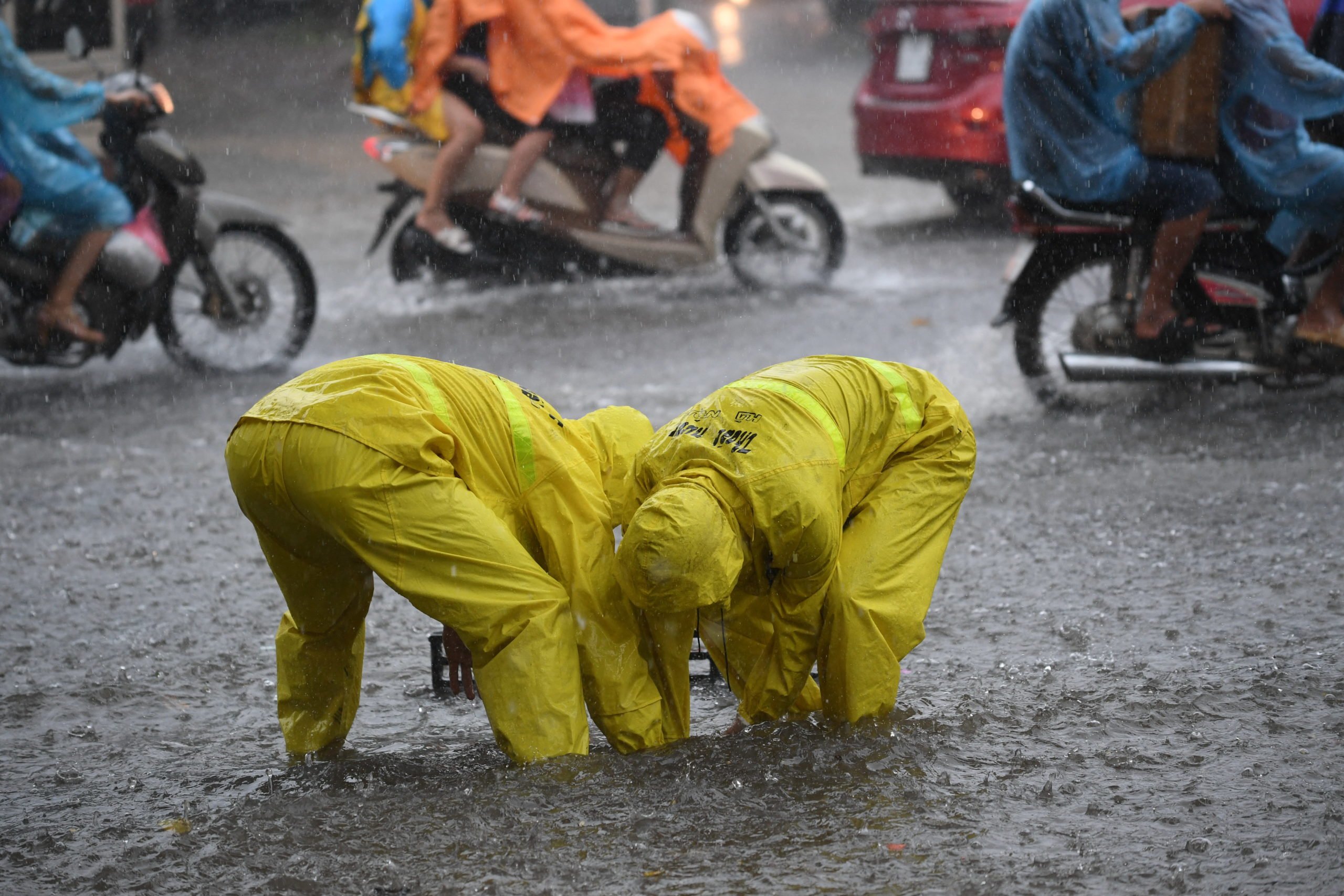 Two workers from the municipal drainage company open a sewer on a flooded street in Hanoi on July 17, 2017, after tropical storm Talas made landfall in northern Vietnam. (Photo by HOANG DINH NAM/AFP via Getty Images)