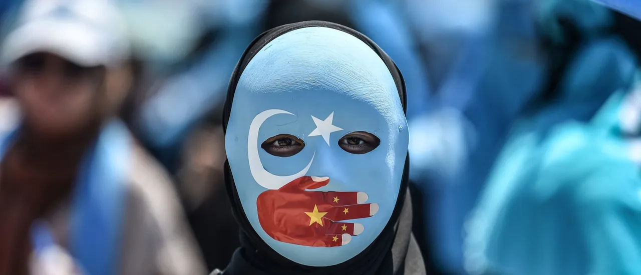 A demonstrator wearing a mask painted with the colors of the flag of East Turkestan and a hand bearing the colors of the Chinese flag attends a protest of supporters of the mostly Muslim Uighur minority and Turkish nationalists to denounce China's treatment of ethnic Uighur Muslims during a deadly riot in July 2009 in Urumqi, in front of the Chinese consulate in Istanbul, on July 5, 2018. (Photo by OZAN KOSE/AFP via Getty Images)
