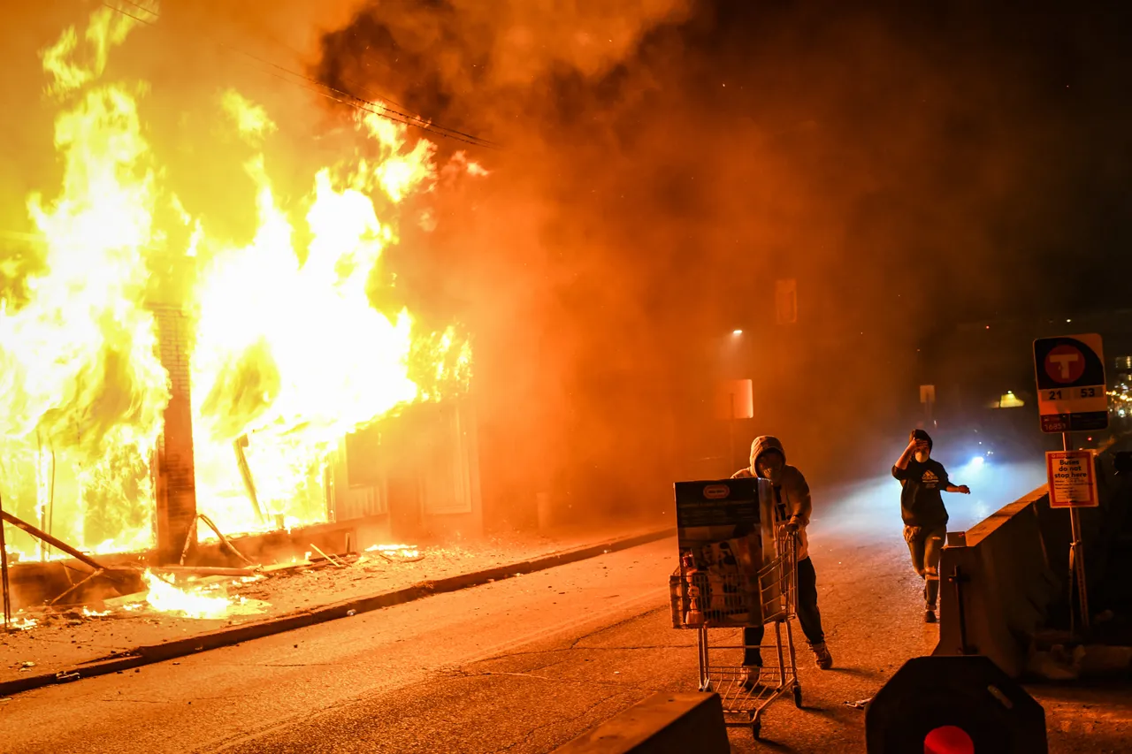 People walk in front of a burning building in Minneapolis, United States on May 30, 2020 during unrest resulting from the killing of an unarmed black man, George Floyd, by police.