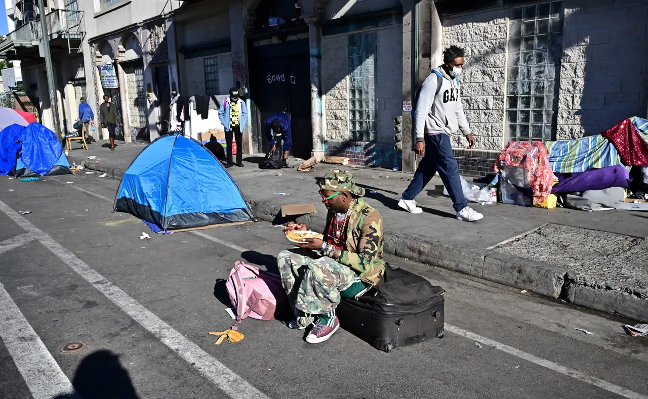 TOPSHOT - A homeless man sits on a luggage bag along a downtown Los Angeles street lined with tents housing the homeless on November 22, 2023 in Los Angeles, California, where skyrocketing rents in recent years has led to an increasing rise in the number of unhoused people. Some 75,500 people live on the streets of Los Angeles and its sprawling suburbs, according to a January survey. The figure is up 70 percent since 2015, in a city where sometimes shocking levels of inequality are on daily display. (Photo by FREDERIC J. BROWN/AFP via Getty Images)