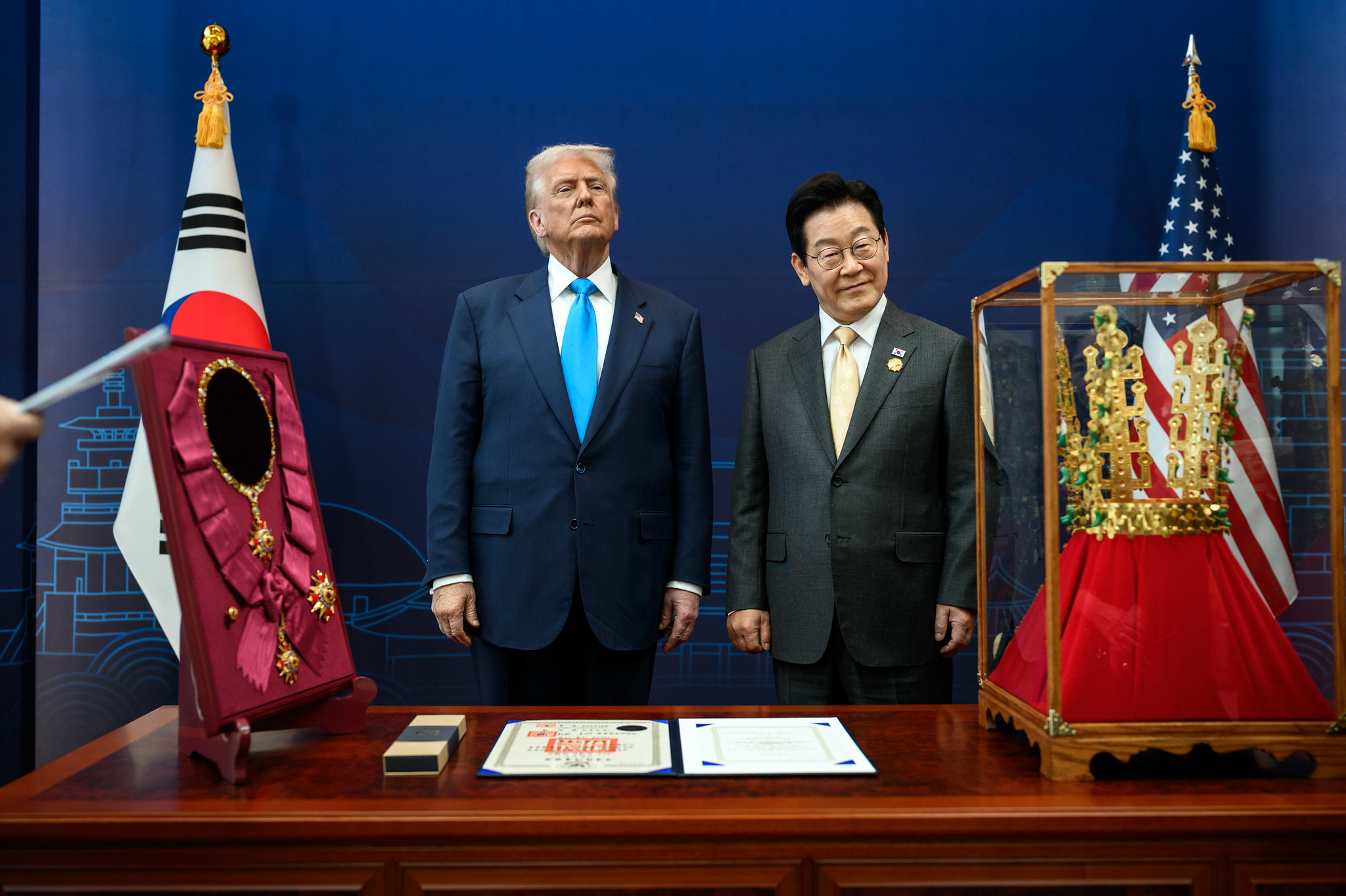 Two men stand near ceremonial objects and flags.