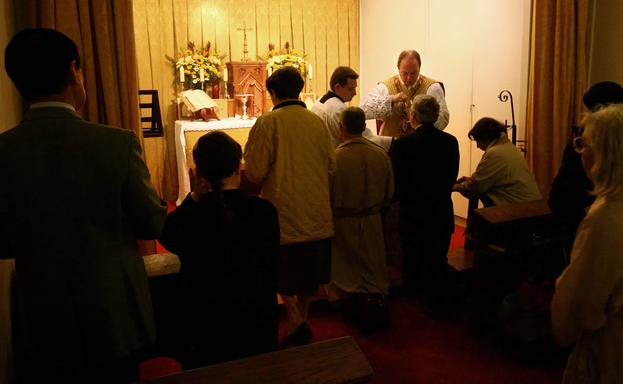 L'abbé traditionaliste de Paris Guillaume de Tanouarn donne la communion à des fidèles à genoux lors d'une messe en latin dans leur centre culturel de Paris, le 29 octobre 2006. (Photo by THOMAS COEX/AFP via Getty Images)