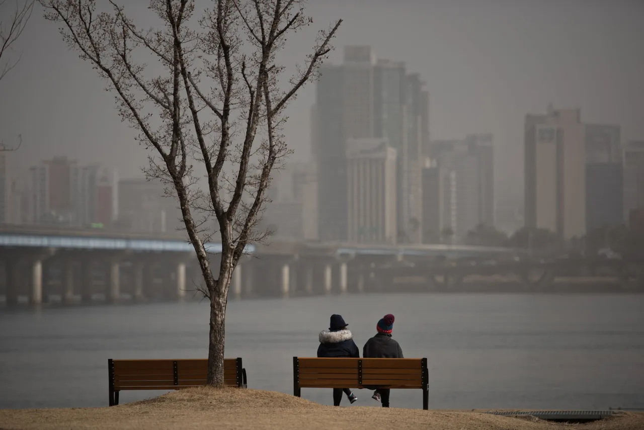 Two people sit on a bench before the Han River and Seoul city skyline during heavily polluted weather on February 23, 2015. (Photo by ED JONES/AFP via Getty Images)