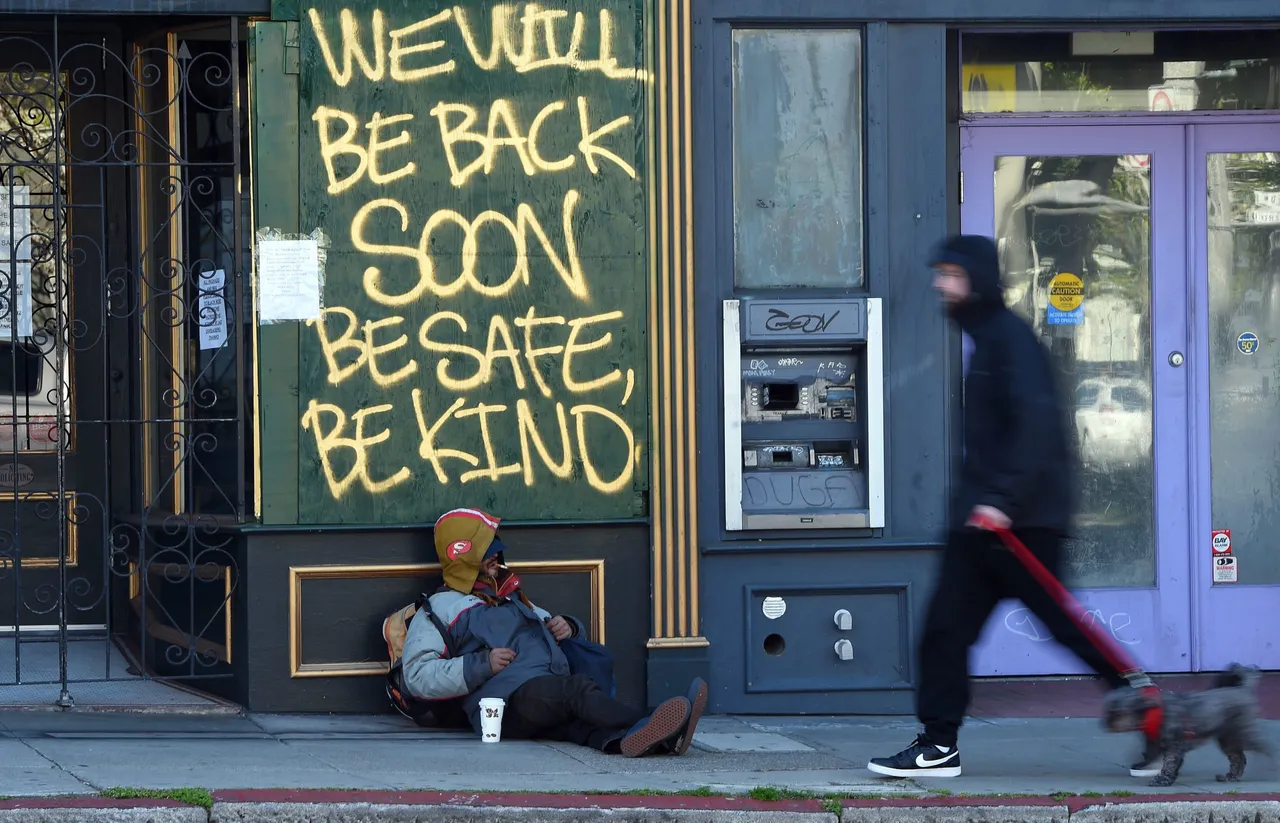 A man walks his dog past a homeless man sleeping under a message painted on a boarded up shop in San Francisco, California on April, 1, 2020. (Photo by JOSH EDELSON/AFP via Getty Images)