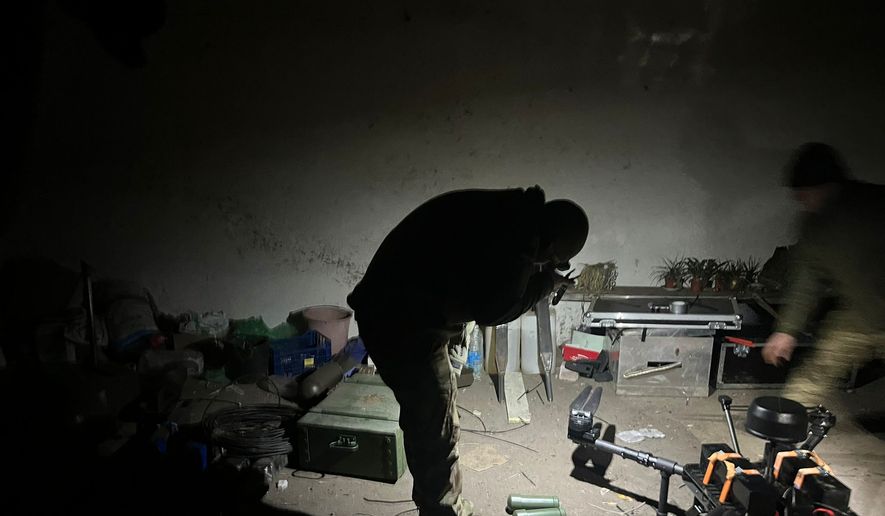 In the basement of a safe house near the frontlines in Ukraine, the crew works on heavy-duty drones, performing maintenance and carefully attaching ordnance. (Guillaume Ptak/The Washington Times).